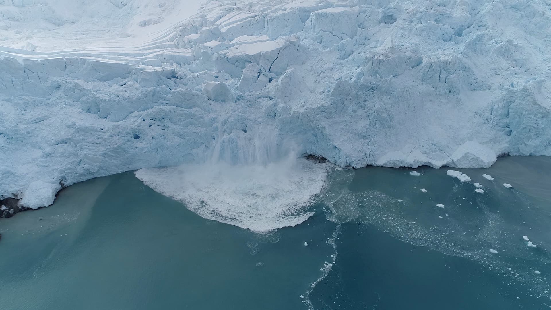 The glacier ice front collapsing into the sea, spray rising from the impact