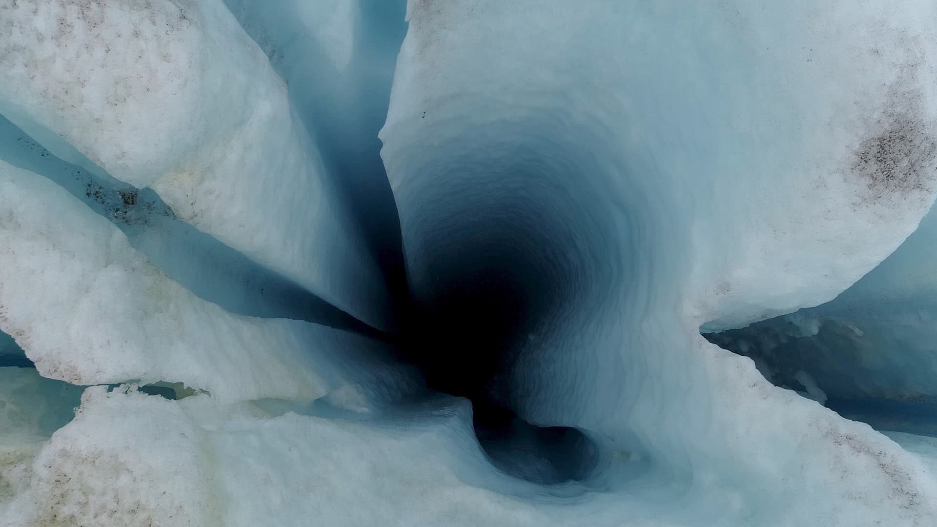 A glacial moulin, a dark meltwater shaft seen from above