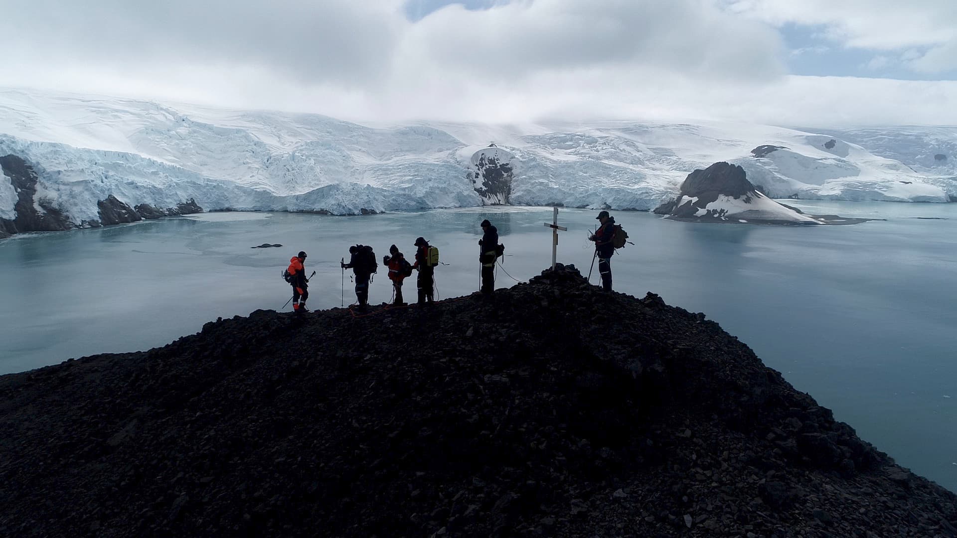 Silhouettes of the team on a ridge, glacier in the background