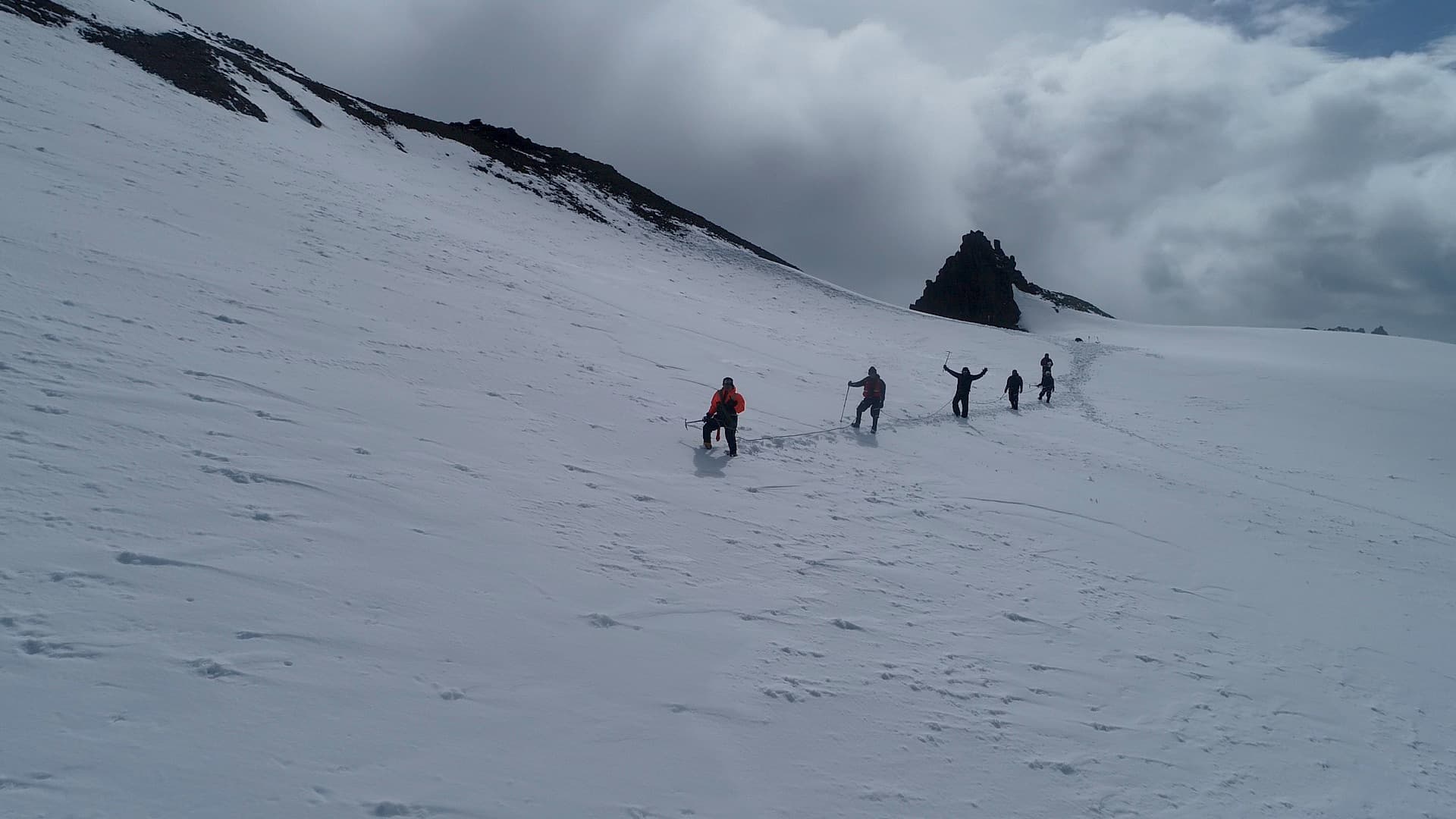 Three researchers in red jackets roped together, traversing the glacier surface on foot