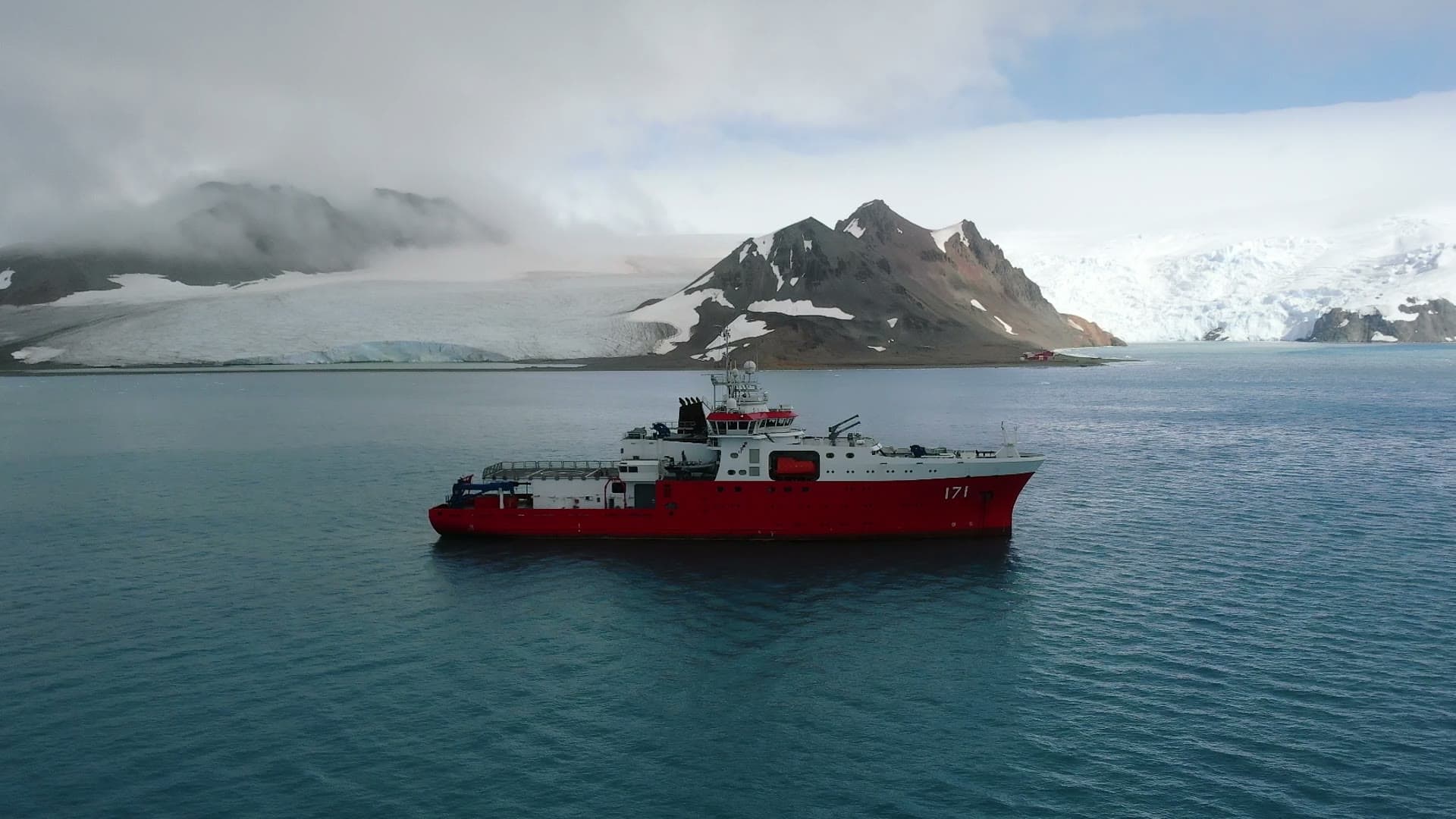 The red research vessel at anchor, mountains and glacier behind